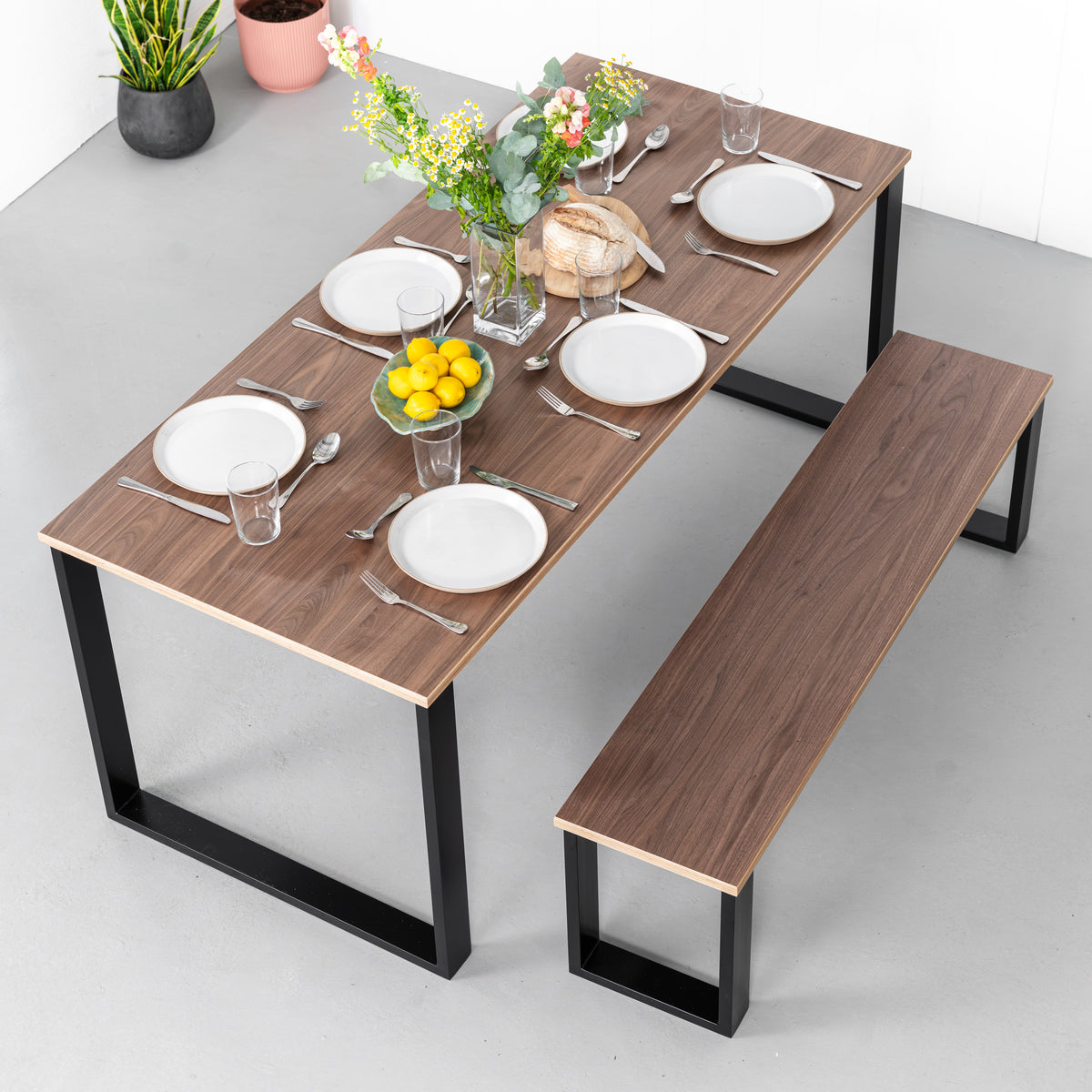 Walnut dining table and matching bench with black Square legs, viewed from above with plates and flowers