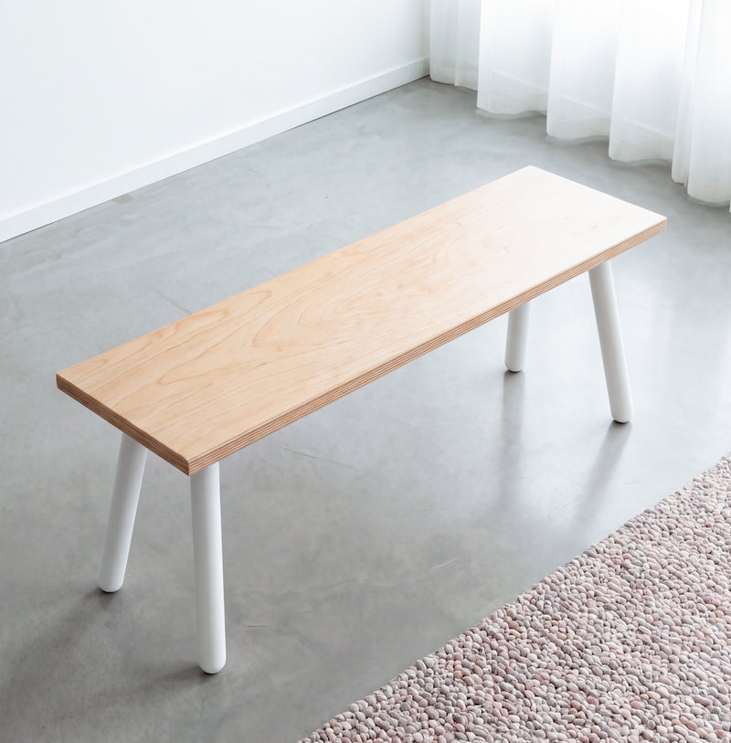 Birch plywood dining bench with white round Single Pin legs, viewed at an angle