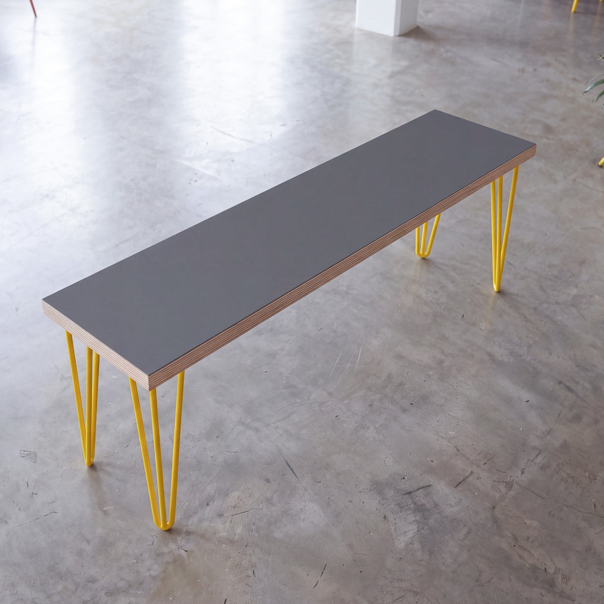 Grey Formica dining bench with yellow hairpin legs, viewed at an angle